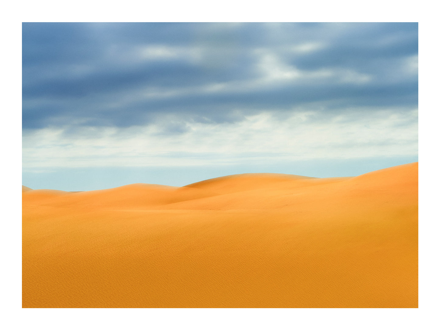 Photograph of deep yellow sand dunes and a blue sky with clouds