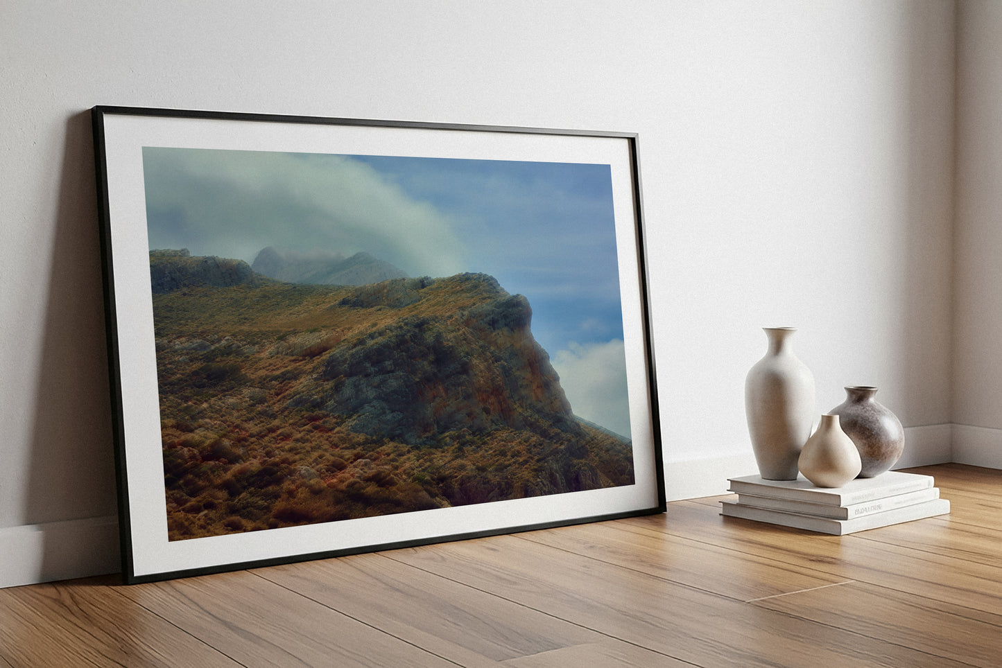 Framed landscape fine art print of a mountainous scene on a wooden floor with decorative vases.
