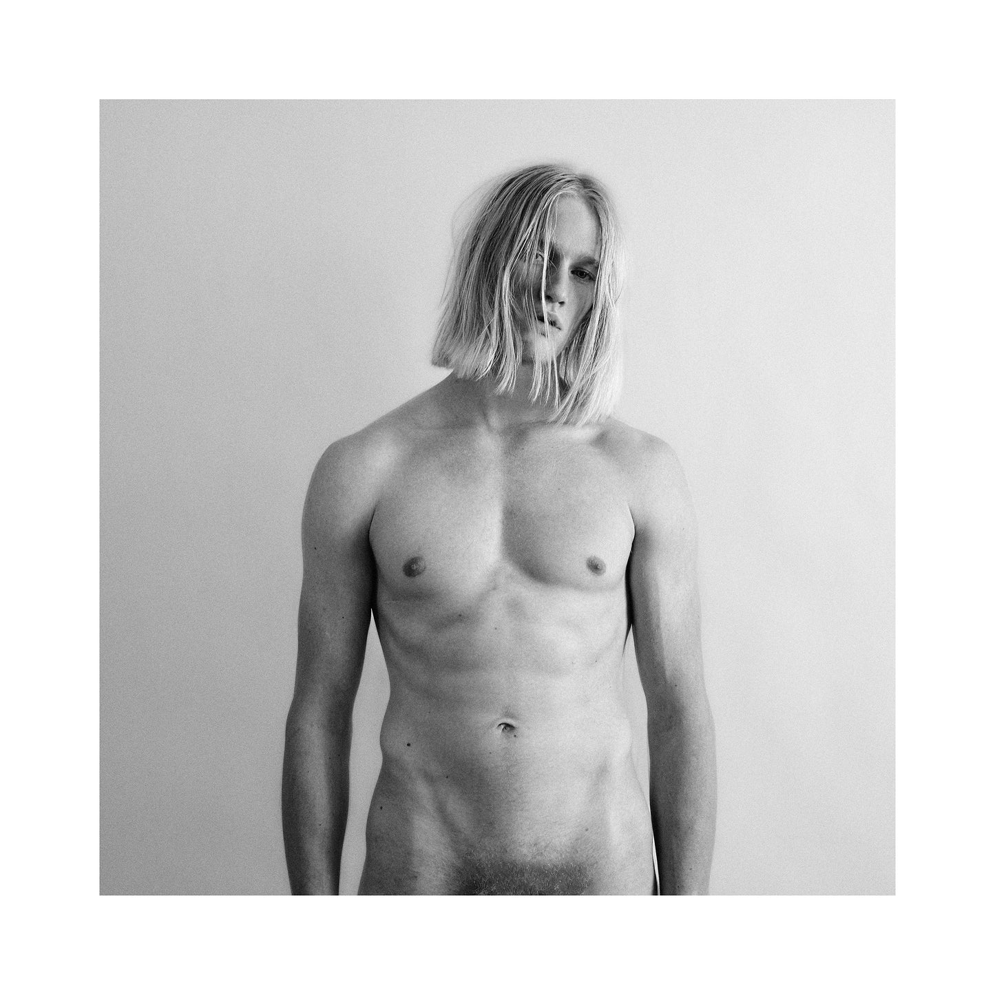 Black and white portrait photo of a shirtless male with long hair against a plain background