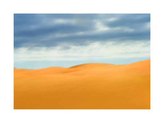 Fine Art Photography of a Desert landscape with orange sand dunes and a blue sky with clouds.