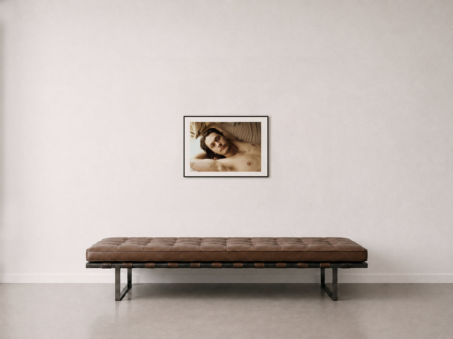 A franed 18" x 24" fine art photograph of a man laying on bed, hanging on a wall above a mid-century daybed.
