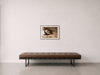 A franed 18" x 24" fine art photograph of a man laying on bed, hanging on a wall above a mid-century daybed.