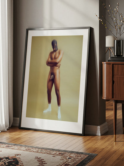 Framed portrait of a nude person on a wall in a room with wooden floor and sideboard.