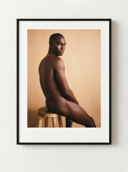 Framed fine art portrait of a nude male sitting on a stool against a beige background