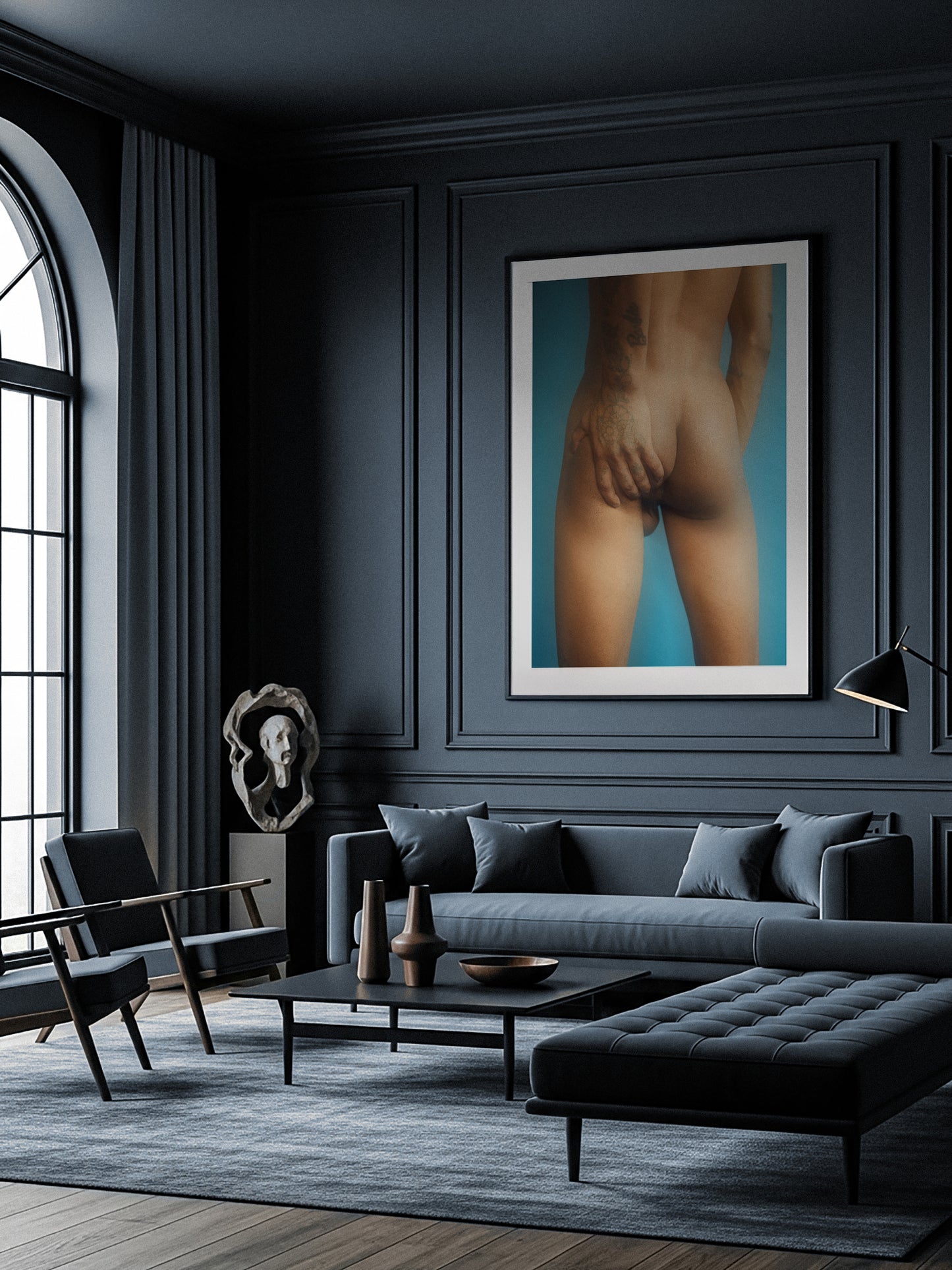 Modern living room with a dark gray sofa, armchair, and coffee table. A framed artwork of a nude figure is displayed on the wall, art by Lucas Castro Pardo