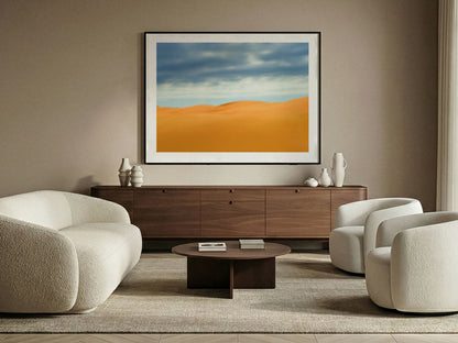 Modern living room with beige sofas, a wooden coffee table, and a fine art photograph of desert dunes landscape on the wall.