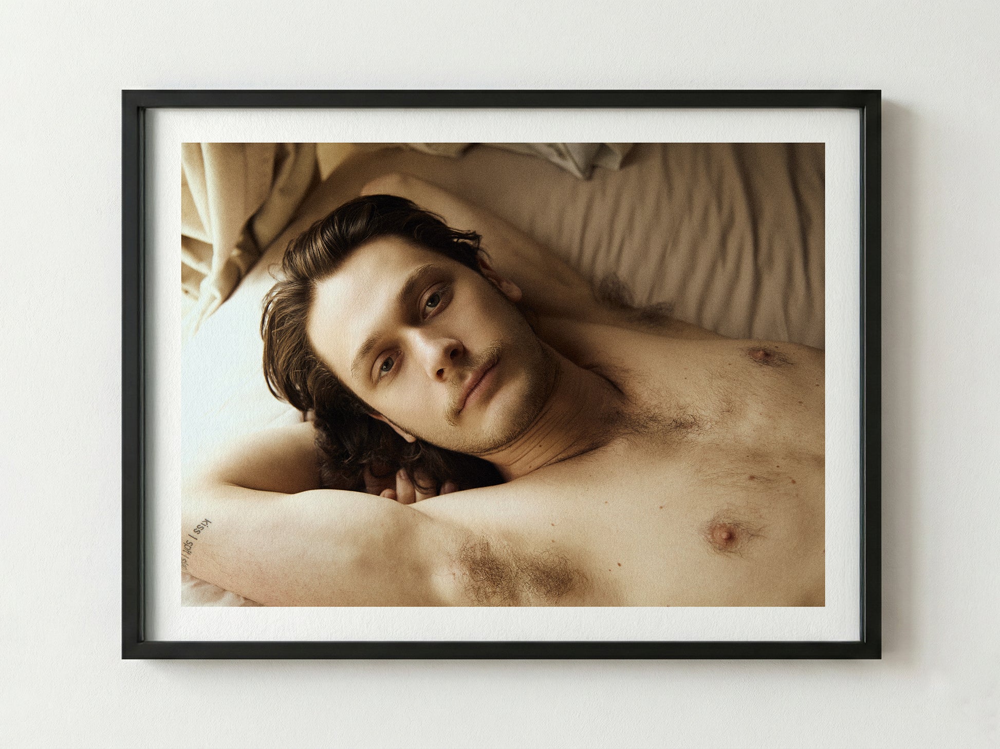 Framed portrait of a shirtless man lying on a bed with a neutral background