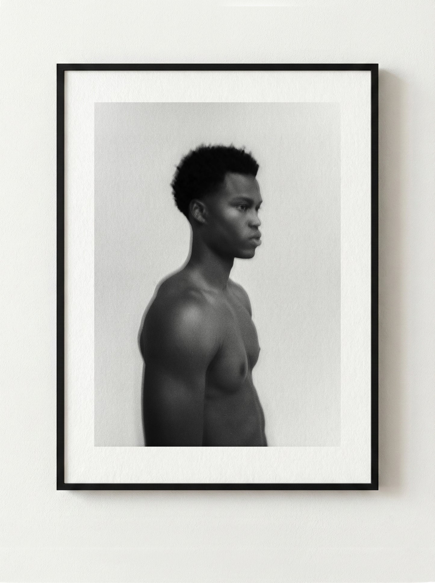 Framed black and white fine art portrait of a shirtless male on a white wall.