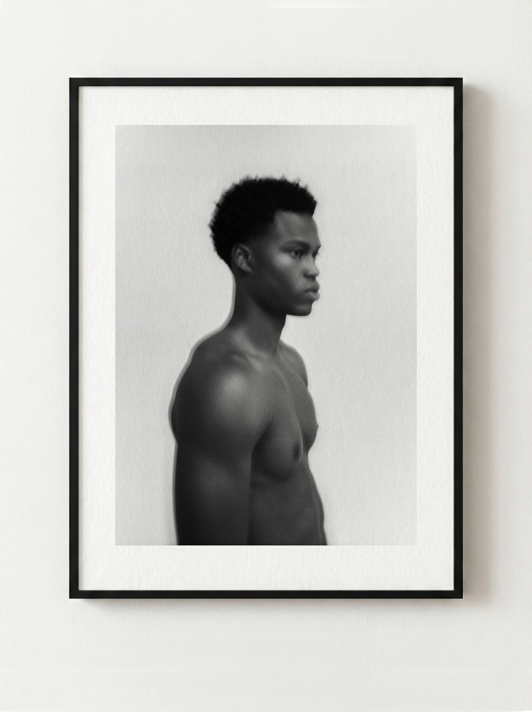 Framed black and white fine art portrait of a shirtless male on a white wall.