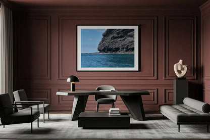 Modern living room with a large framed fine art picture of a coastal scene on a brown wall.