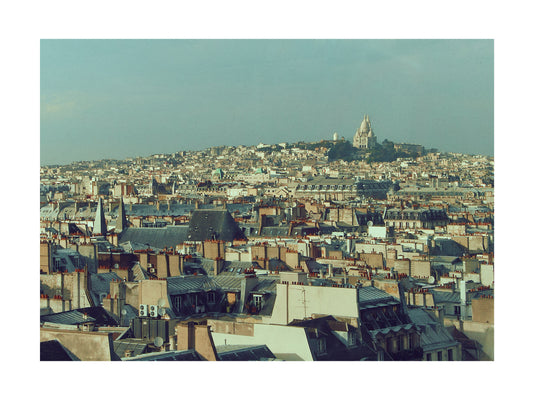 Paris Cityscape with rooftops and Sacre Coeur on a hill under a clear sky.